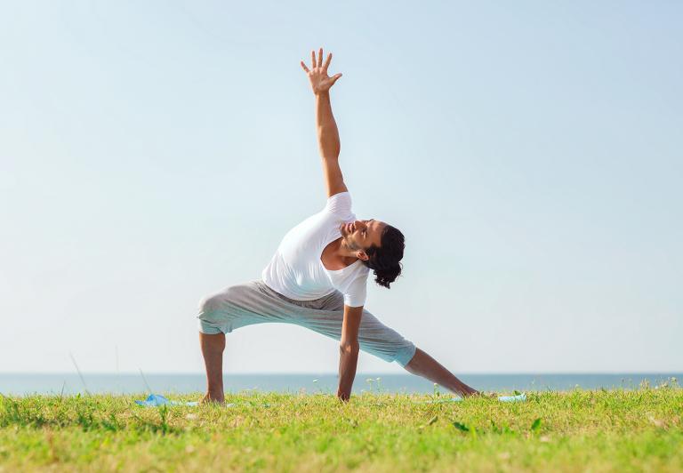 Smiling man doing yoga in the grass.