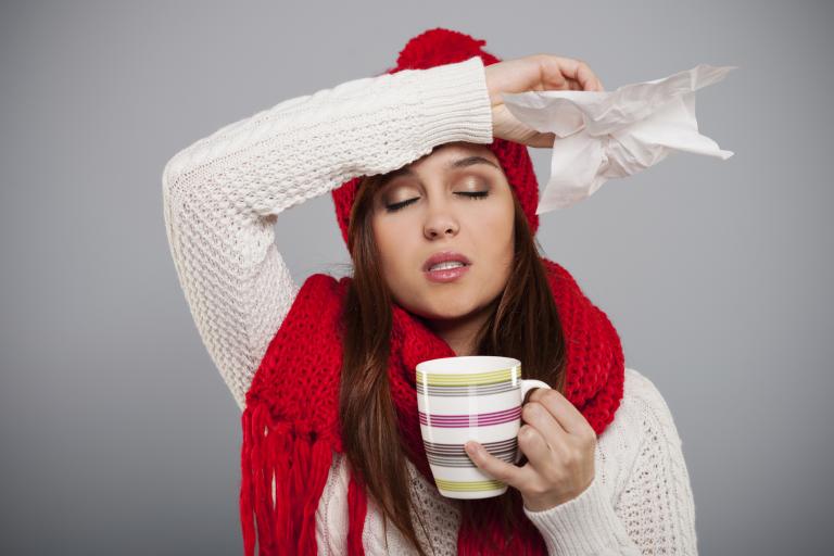 woman in a hat and scarf with a tissue in her hand drinking tea