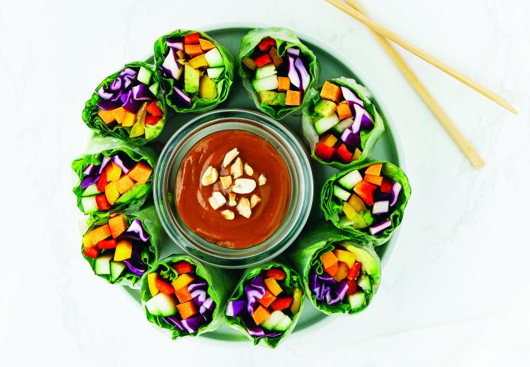 Colorful veggies wrapped in lettuce, positioned vertically around a dish of hoisin sauce.